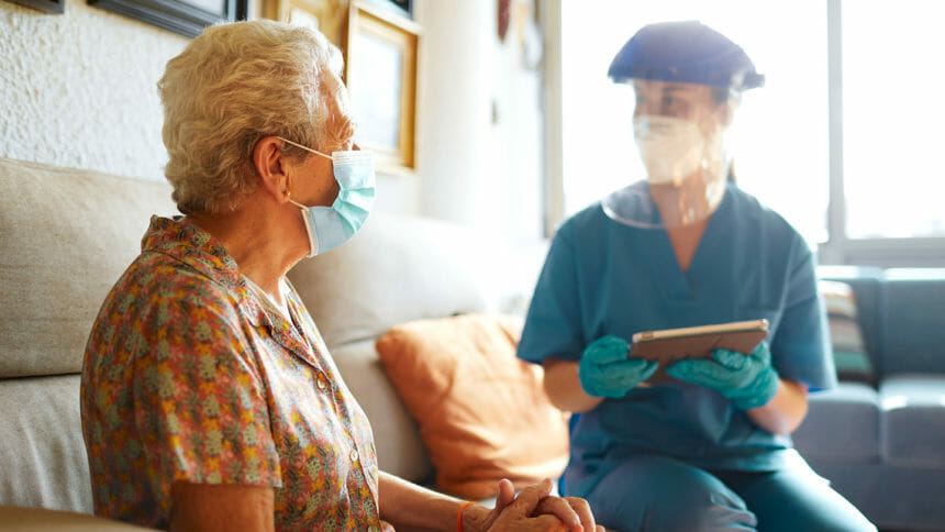 Nurse dressed in personal protective equipment helps a senior woman at a nursing home